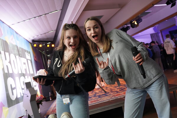 Zwei Mädchen auf dem KonfiCastle zeigen eine Handgeste (Zeige- und kleiner Finger erhoben), um ihre Begeisterung auszudrücken.